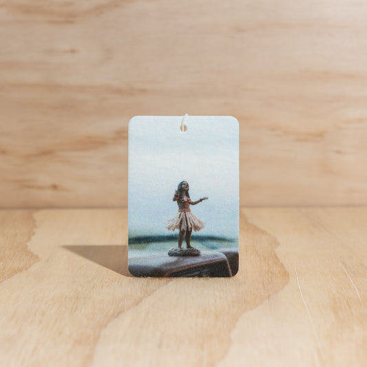 The Commonfolk air freshener features an illustrated hula girl against a beach backdrop.