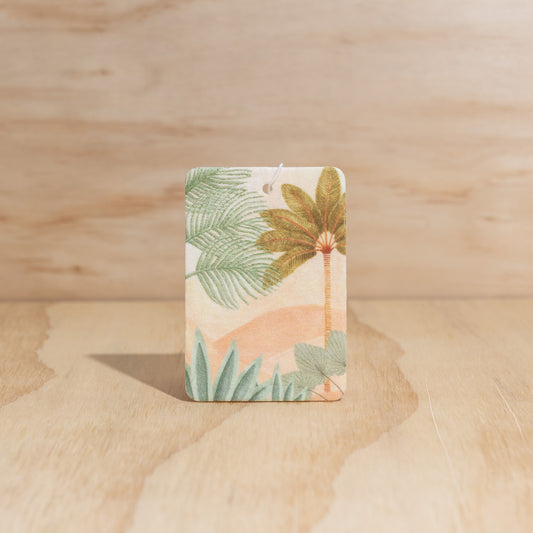 The Commonfolk air freshener, with an artistic print featuring leaves and a mountain, displays on a wooden surface.