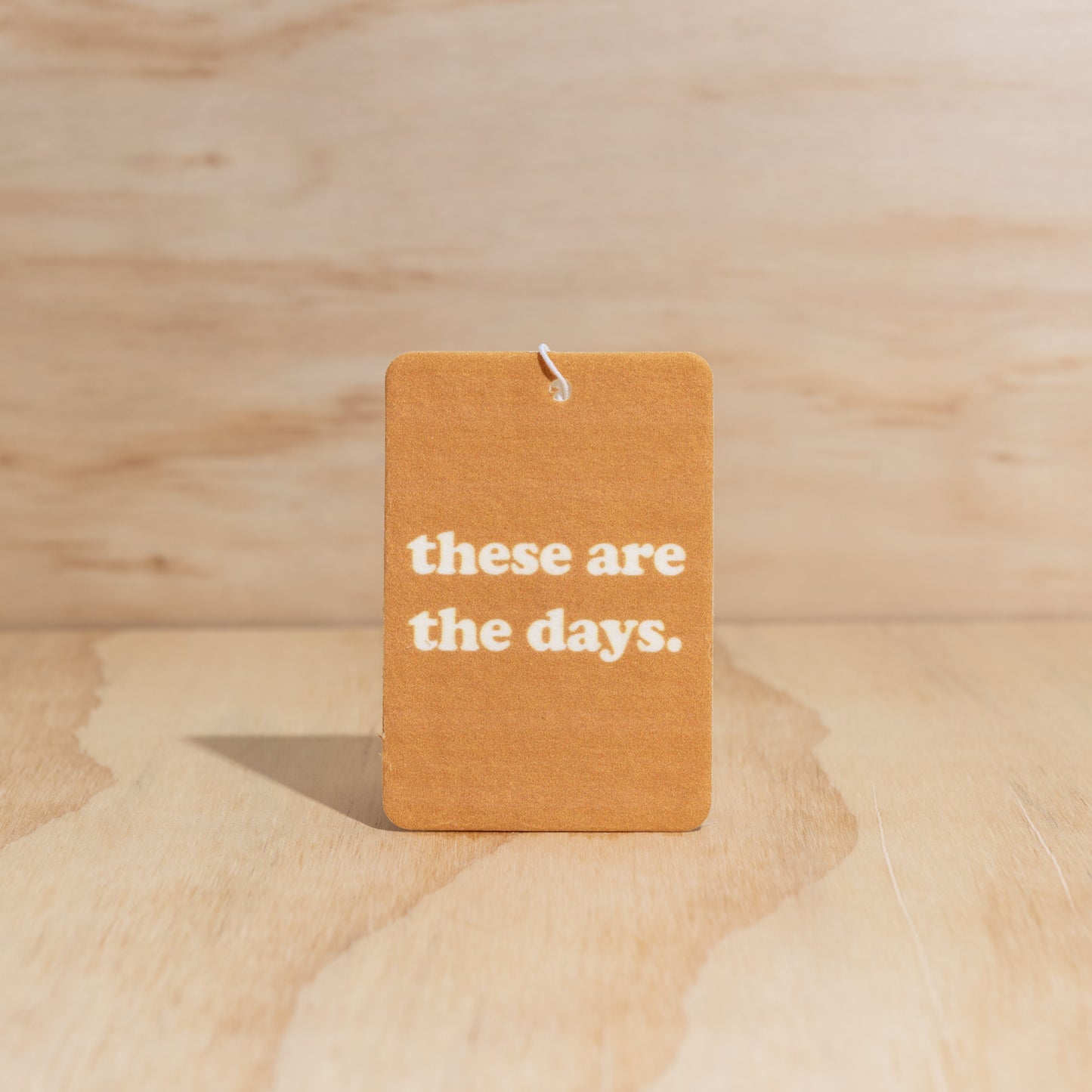The Commonfolk air freshener with the text 'these are the days.' printed in the center, displays on a wooden surface.