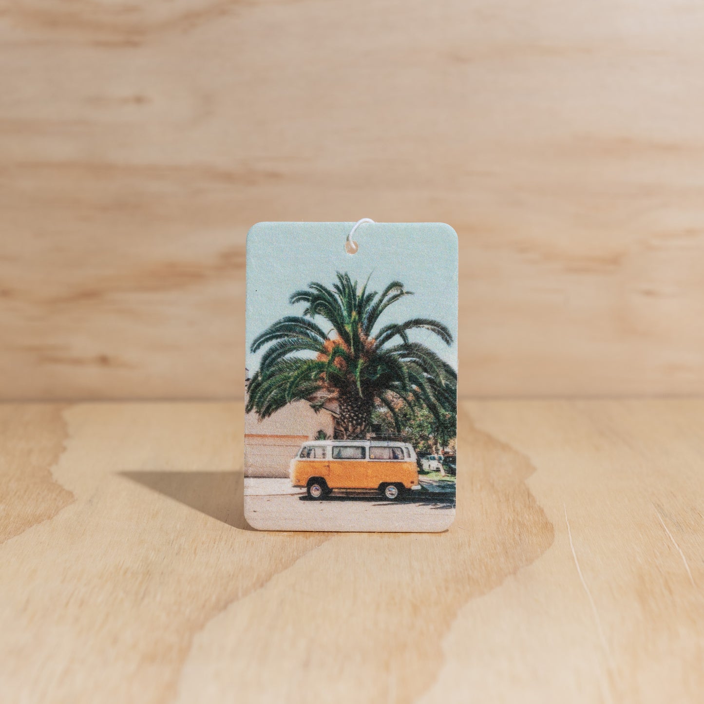 The Commonfolk air freshener, featuring an image of a classic van and palm trees on it, displays against a wooden background.