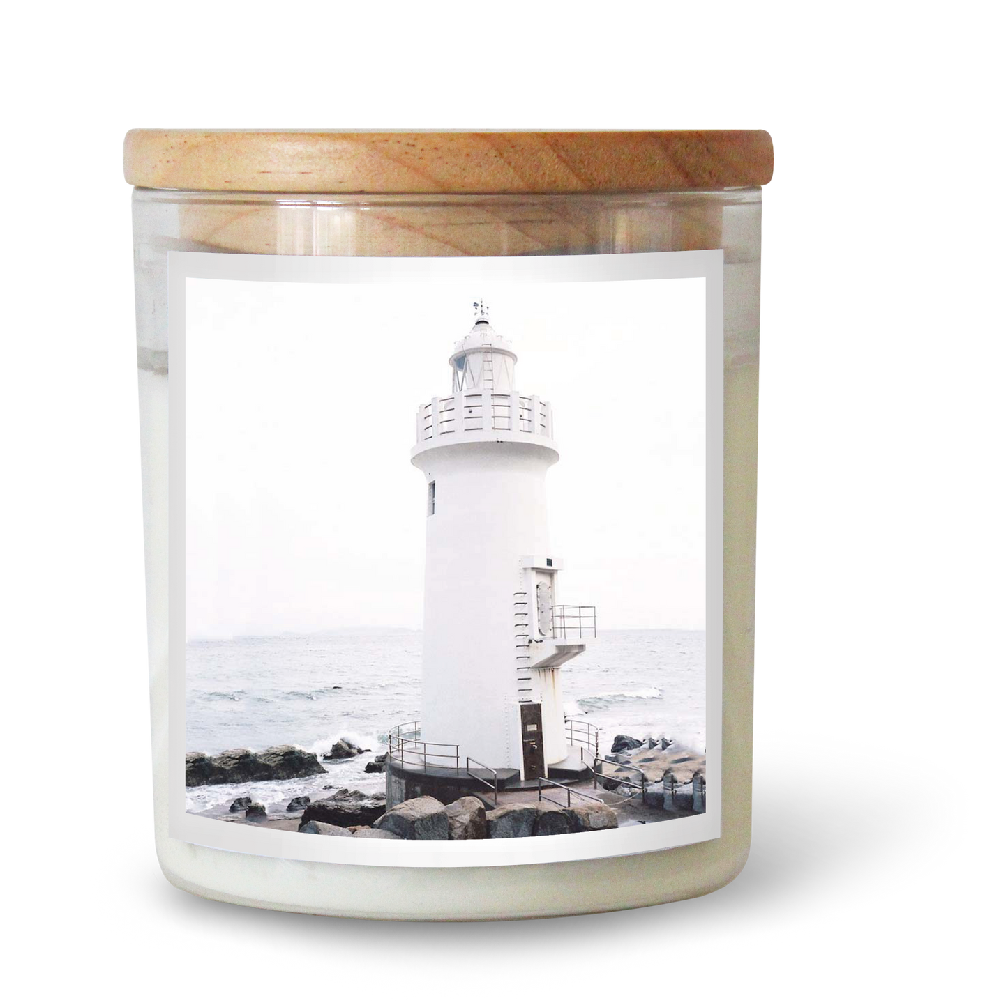 The Commonfolk scented white candle with a lighthouse design is placed in a clear glass jar with a wooden lid.