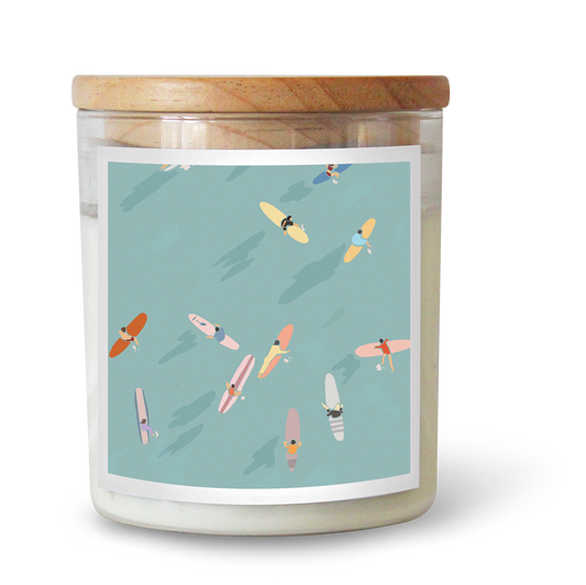 The Commonfolk scented candle features a label with multiple surfboards in various colors on a light blue background, topped with a wooden lid.