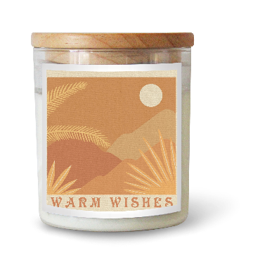 The Commonfolk scented white candle has a beige label featuring mountain and plant graphics, along with the text 'WARM WISHES'. It has a wooden lid on top.