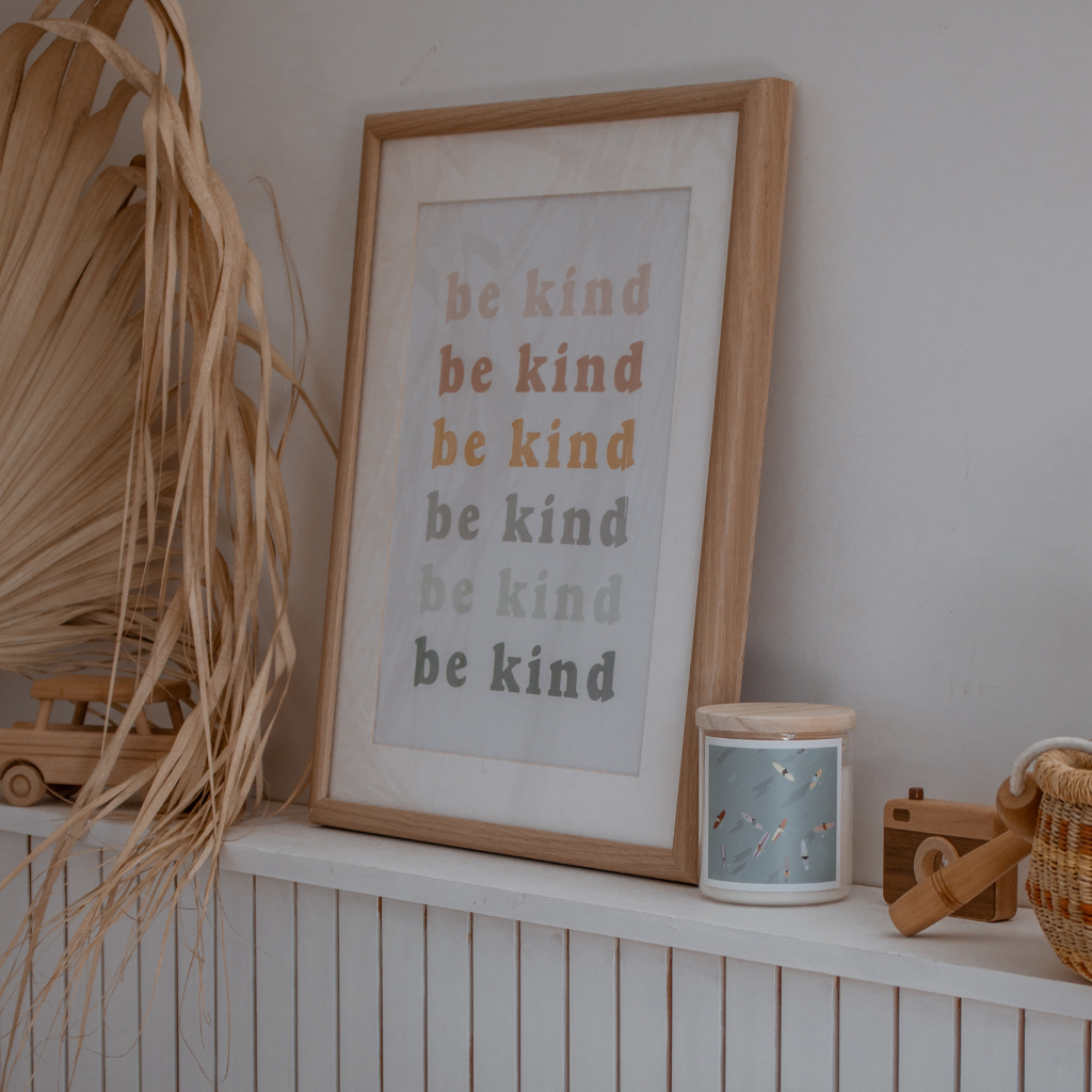 Text repeating "be kind" in a colorful, playful font on a light background, with a scented candle on the side promoting kindness and positivity.