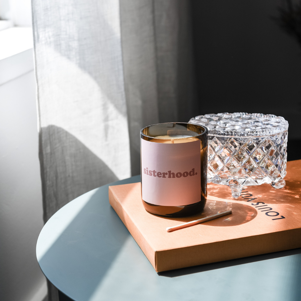 An open candle with an amber jar color sits at the top of the blue table, accompanied by a branded box.