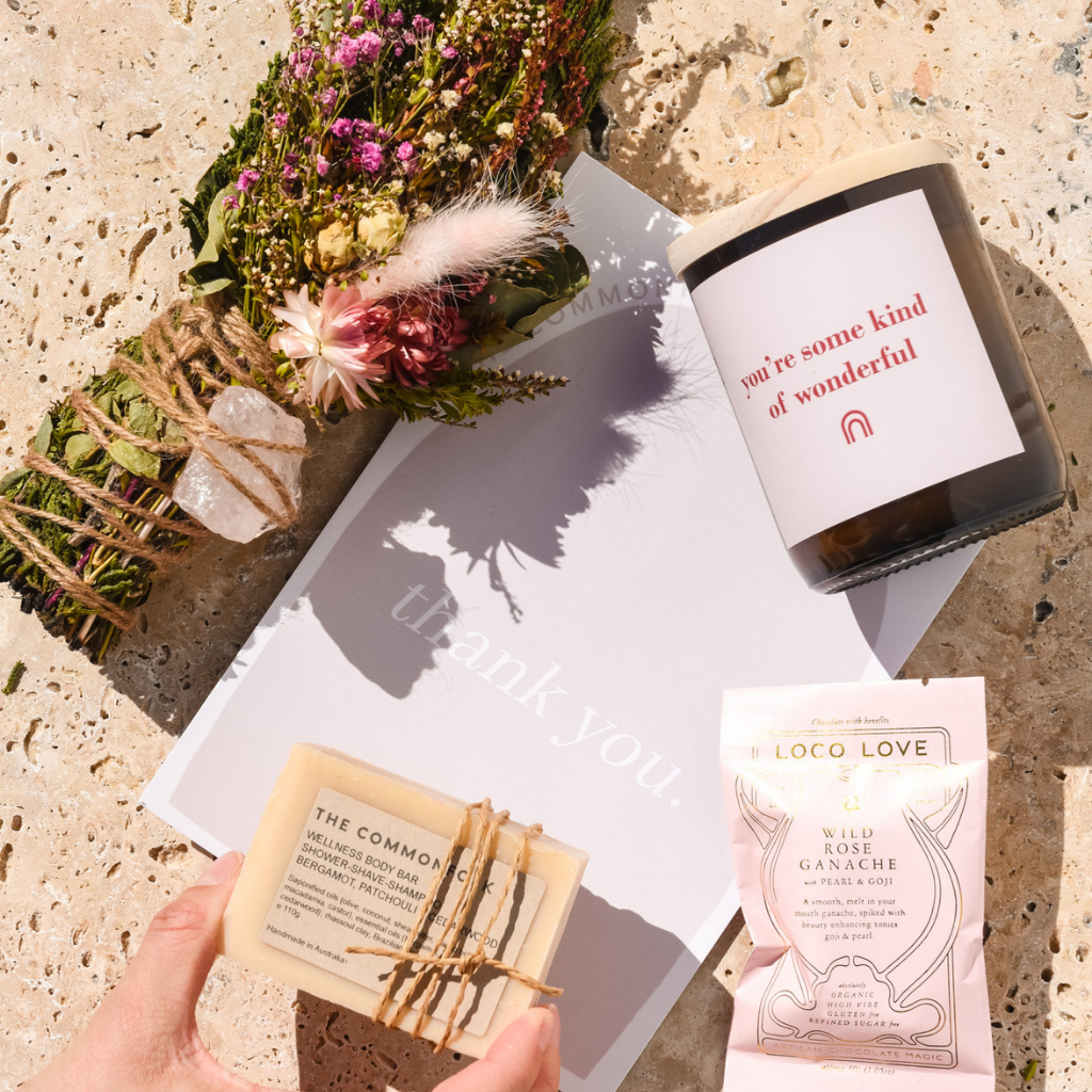 A hand holding a soap, a candle, and a greeting card on a neutral background.