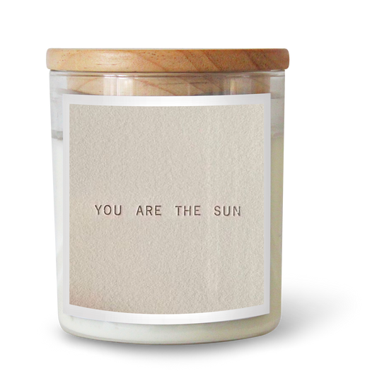 The Commonfolk scented white candle with a label that reads 'YOU ARE THE SUN', contained in a clear glass jar with a wooden lid.