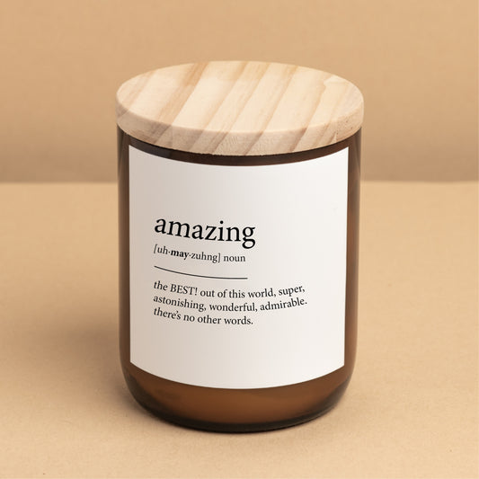 The Commonfolk scented candle with a white label that defines the word 'amazing,' placed on a brown jar with a wooden lid.