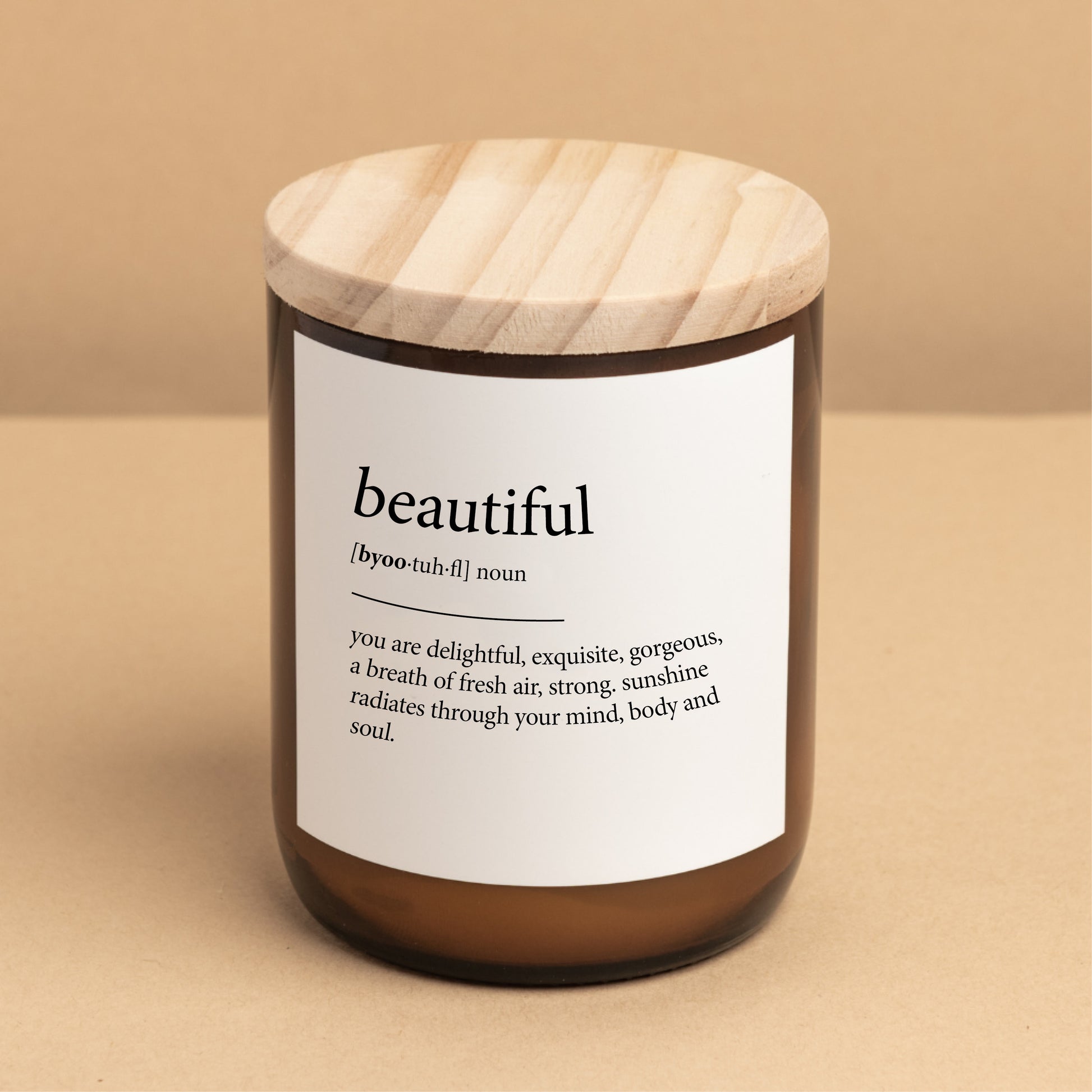 The Commonfolk scented candle with a wooden lid, a white label with the word 'beautiful' printed on it, and a definition in brackets.