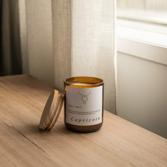 The Commonfolk scented soy wax candle with a Capricorn zodiac sign on it, placed on a wooden surface, with the lid beside it.