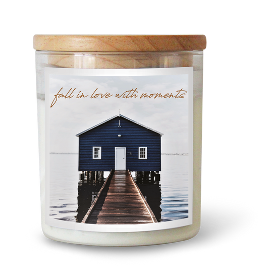 The Commonfolk scented candle features a label with an image of a boathouse and the text "fall in love with moments." The candle has a wooden lid and is included in the product category of soul candles.