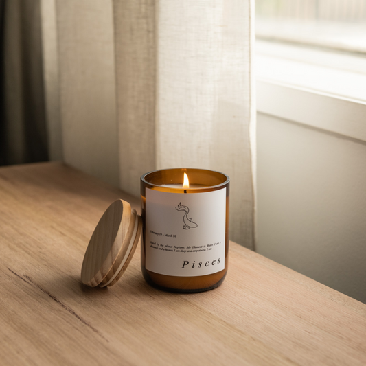 The Commonfolk scented candle with a label that reads 'Pisces', placed on a wooden surface, with the lid of the candle visible to the left of the frame.
