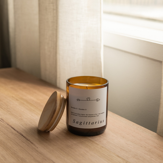 The Commonfolk scented soy wax candle with a wooden lid, labeled 'Sagittarius', placed on a wooden surface with natural lighting from a window in the background.