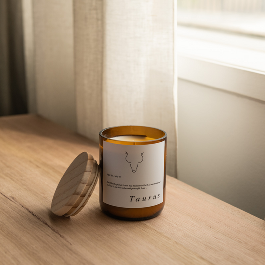 The Commonfolk scented soy wax candle with a wooden lid, labeled 'Taurus', placed on a wooden surface, with natural lighting in the background.