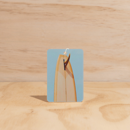 The Commonfolk air freshener, made from post-consumer materials, is displayed on a wooden surface with a mustard tail.