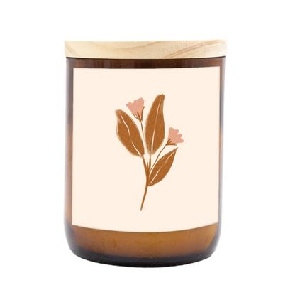 The Commonfolk scented mid-sized candle has a floral design on its label, featuring a predominantly white background with a single flower illustration towards the bottom.