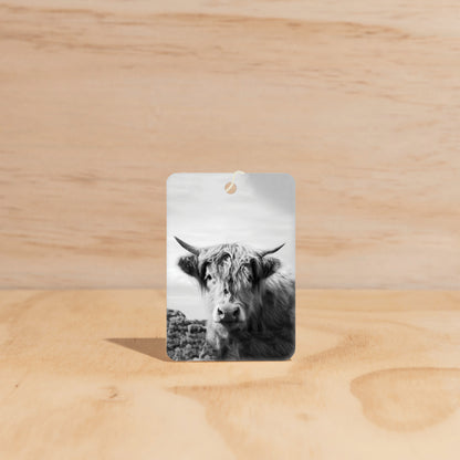 The Commonfolk air freshener featuring a black and white photo of a cow on a wooden surface.