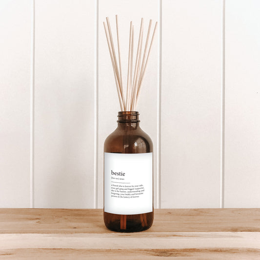 The Commonfolk room diffuser with reeds on a wooden surface and a white wall background, with text that reads 'bestie' with meaning.