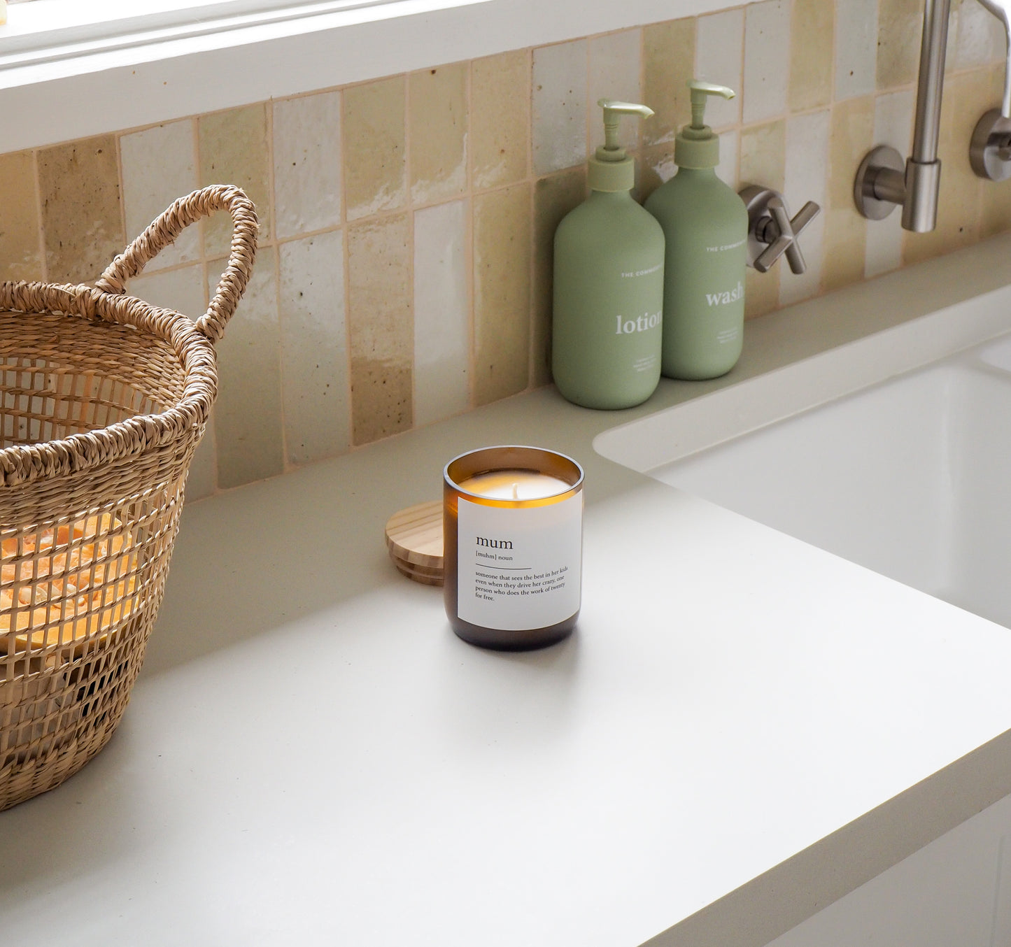 Candle labeled 'mum' on a bathroom counter with soap dispensers and a basket.