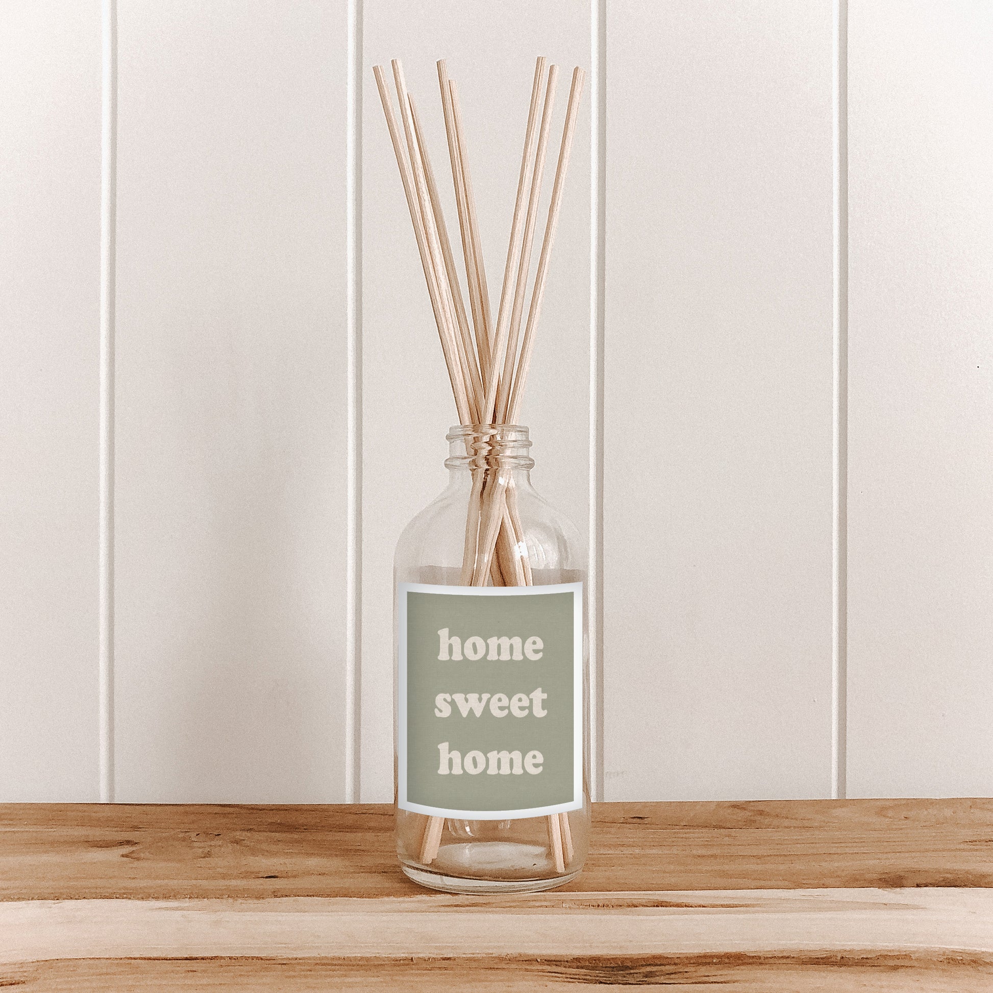 The Commonfolk room diffuser with reeds and 'home sweet home' label on a wooden surface and white paneled wall background