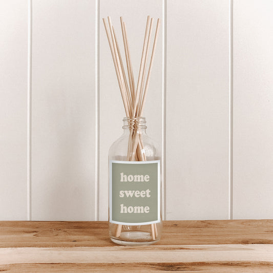 The Commonfolk room diffuser with reeds and 'home sweet home' label on a wooden surface and white paneled wall background