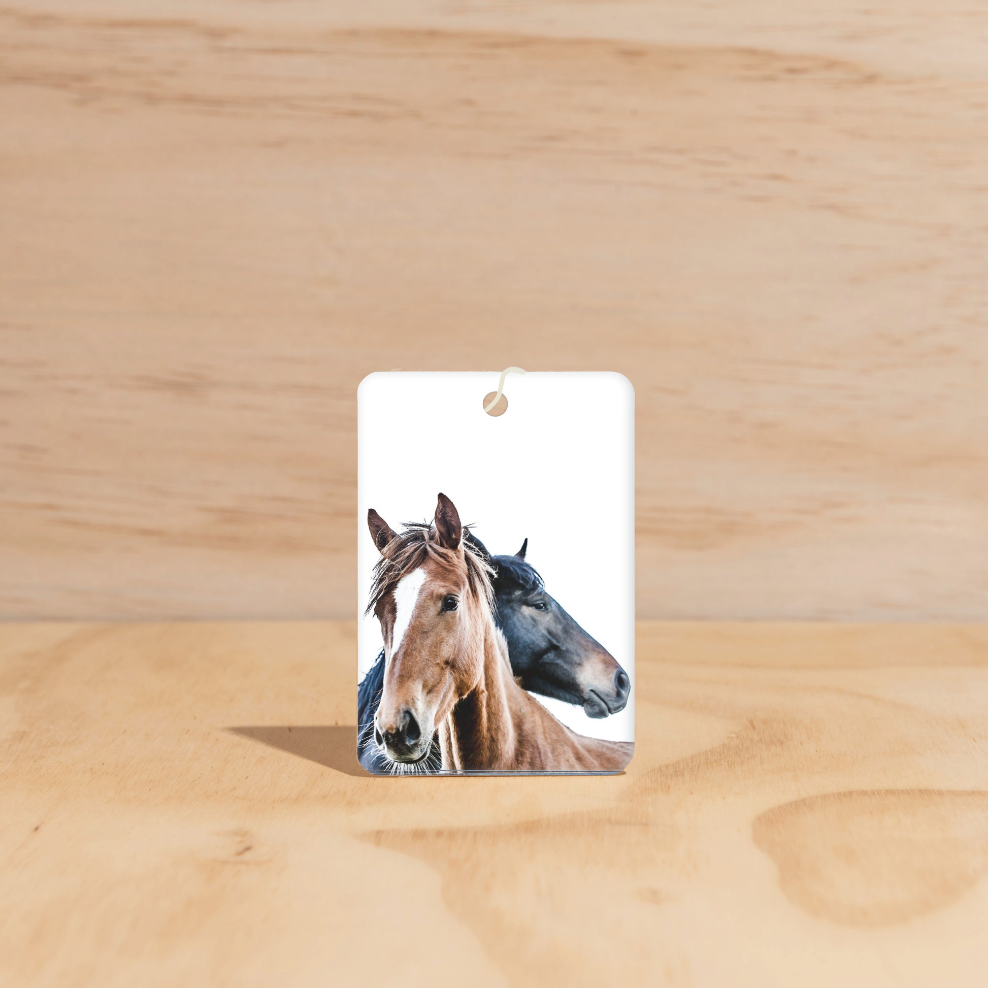 The Commonfolk air freshener featuring two horses’ faces on a wooden surface.