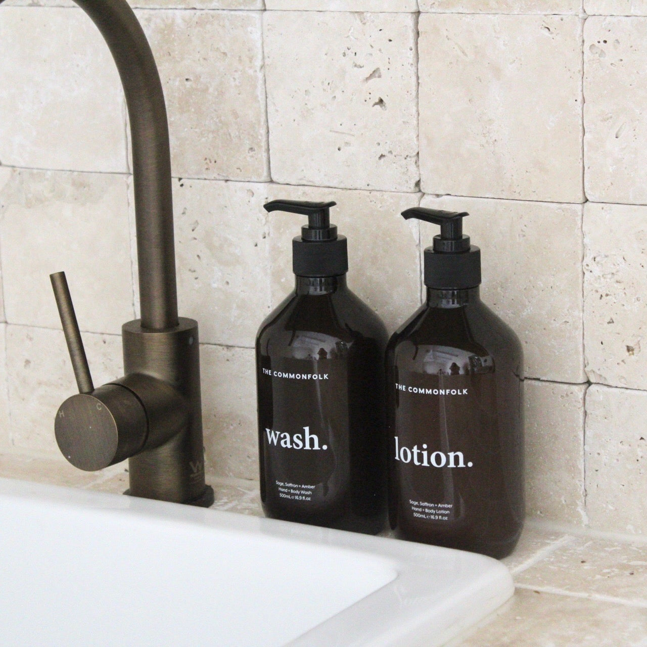 Two amber bottles labeled 'wash' and 'lotion' duo on a sink with a tiled wall background.