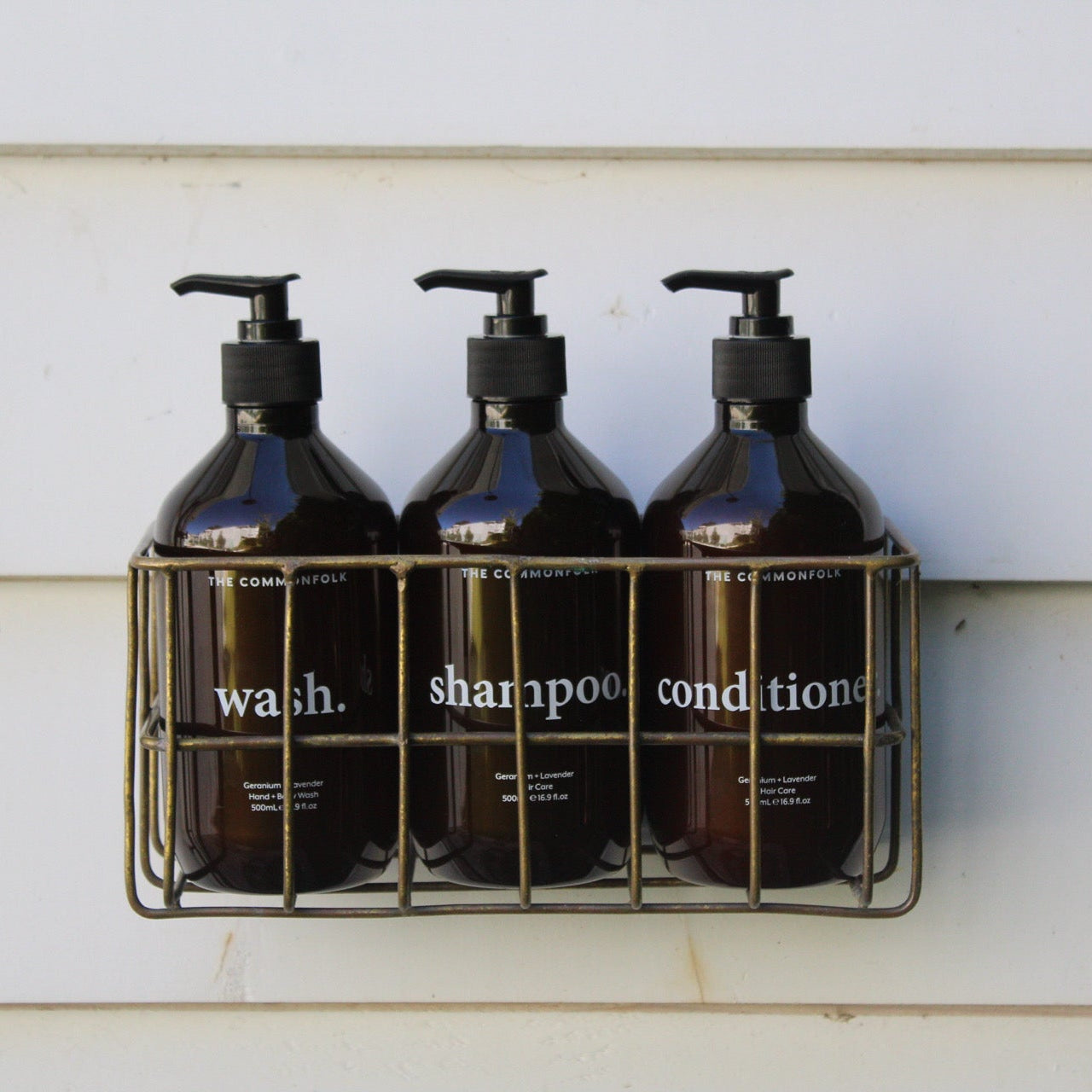 Three amber bottles wash, shampoo, conditioner in outdoor shower weatherboards