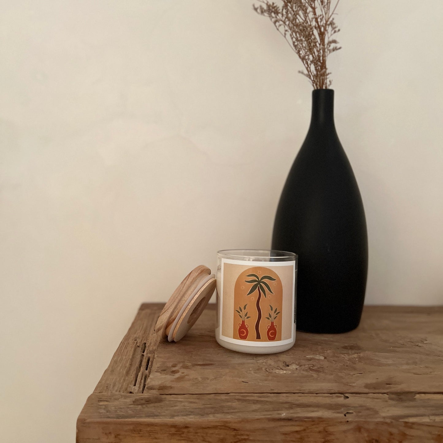 Candle with a decorative design on a wooden table next to a black vase.