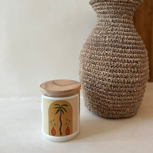 A candle placed beside a vase containing palm trees, creating a serene and tropical ambiance.
