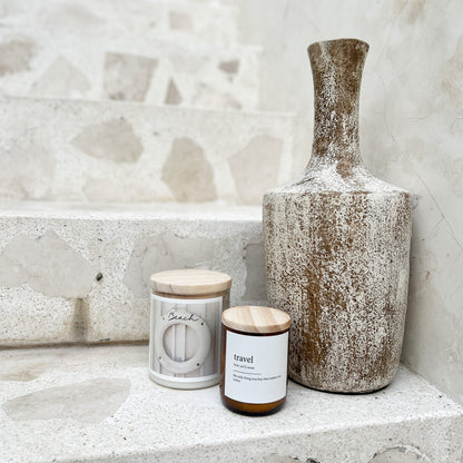 Two candles and a textured vase on a stone surface with a marble wall background