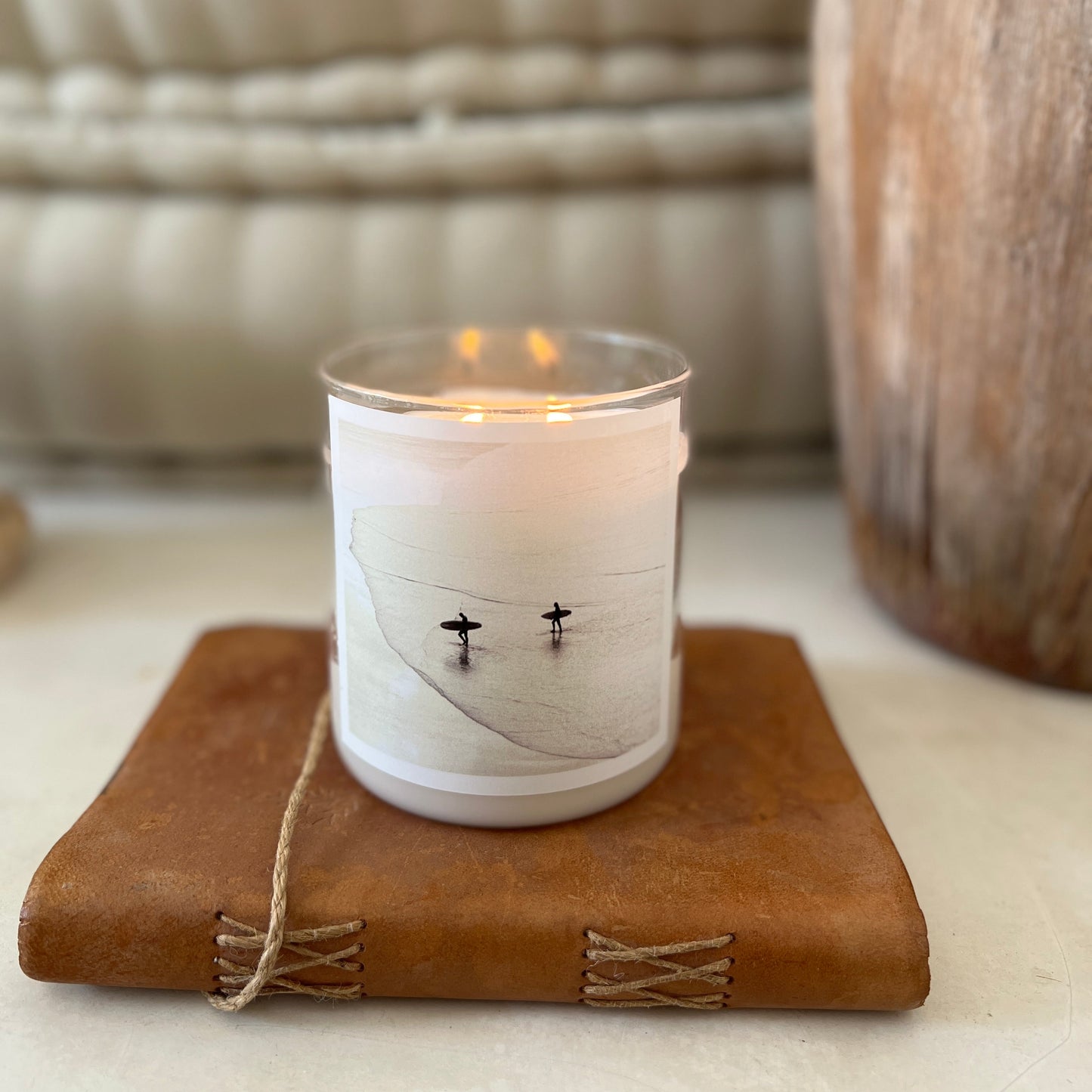 Candle in a white holder with a label on a brown leather surface, blurred background