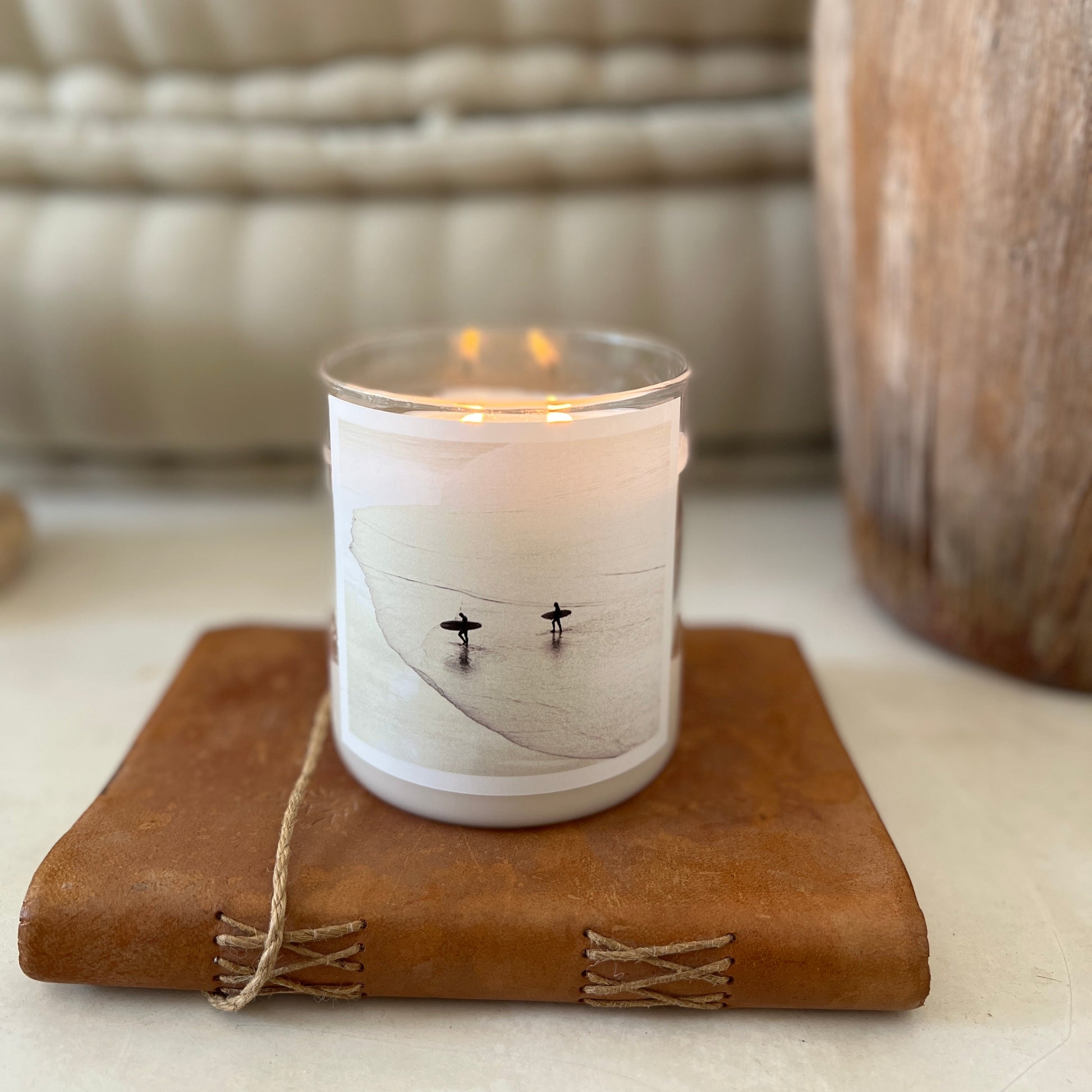 Candle in a white holder with a label on a brown leather surface, blurred background