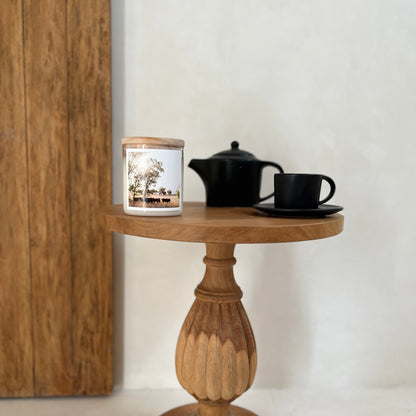 Wooden side table with a candle, teapot, and cup against a white wall.