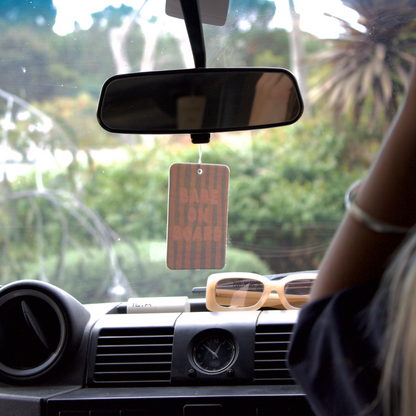 Car interior with a hanging air freshener and a person's arm visible
