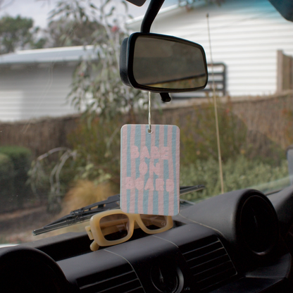 Car dashboard with a hanging air freshener, sunglasses, and rearview mirror.