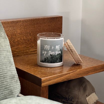 Candle with a label on a wooden surface next to a cap and towel