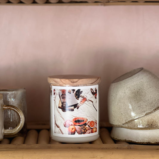 Candle with a decorative label on a wooden shelf with other ceramic items