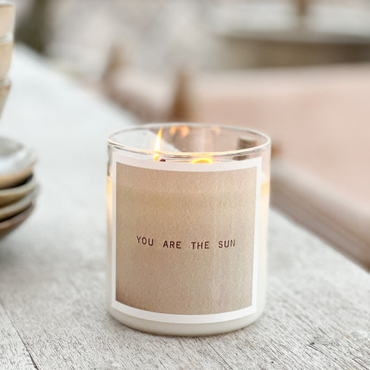 Candle with 'You are the sun' label on a wooden surface