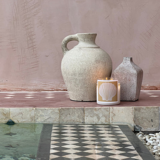 Two stone vases and a candle on a ledge near a pool with a textured wall background.