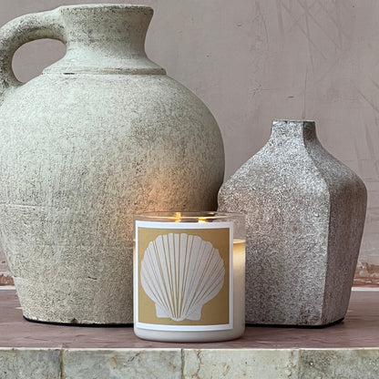 Two stone vases with a candle featuring a shell design on a neutral background