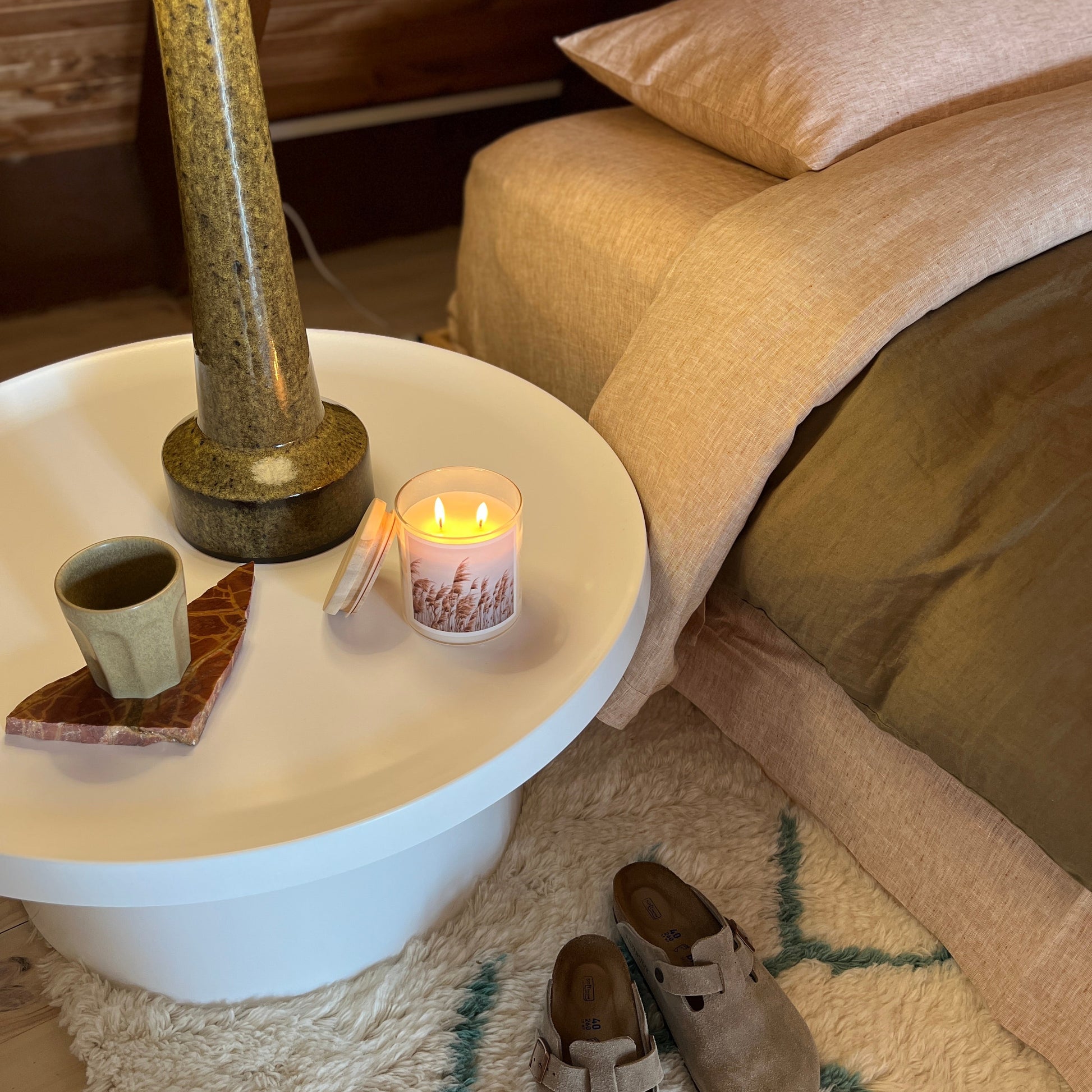 Cozy living room with a small table, candle, and slippers on a rug.