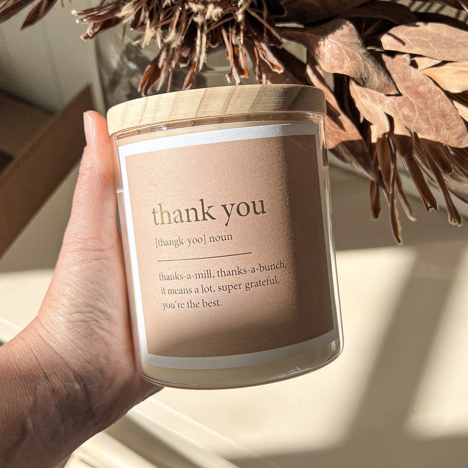 Thank you candle with a warm glow, featuring a "Thank You" label on a rustic wooden table.