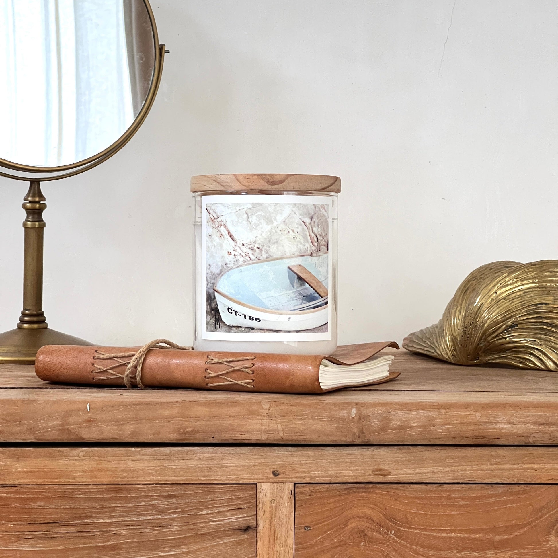 Wooden dresser with a framed picture, rolled leather, and decorative shell on a white wall.