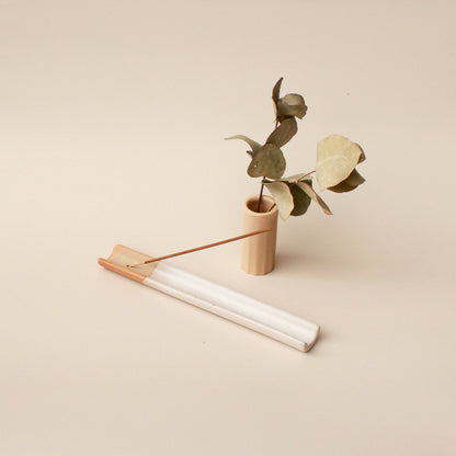 A wooden vase containing a green plant and an incense stick standing in an incense holder.