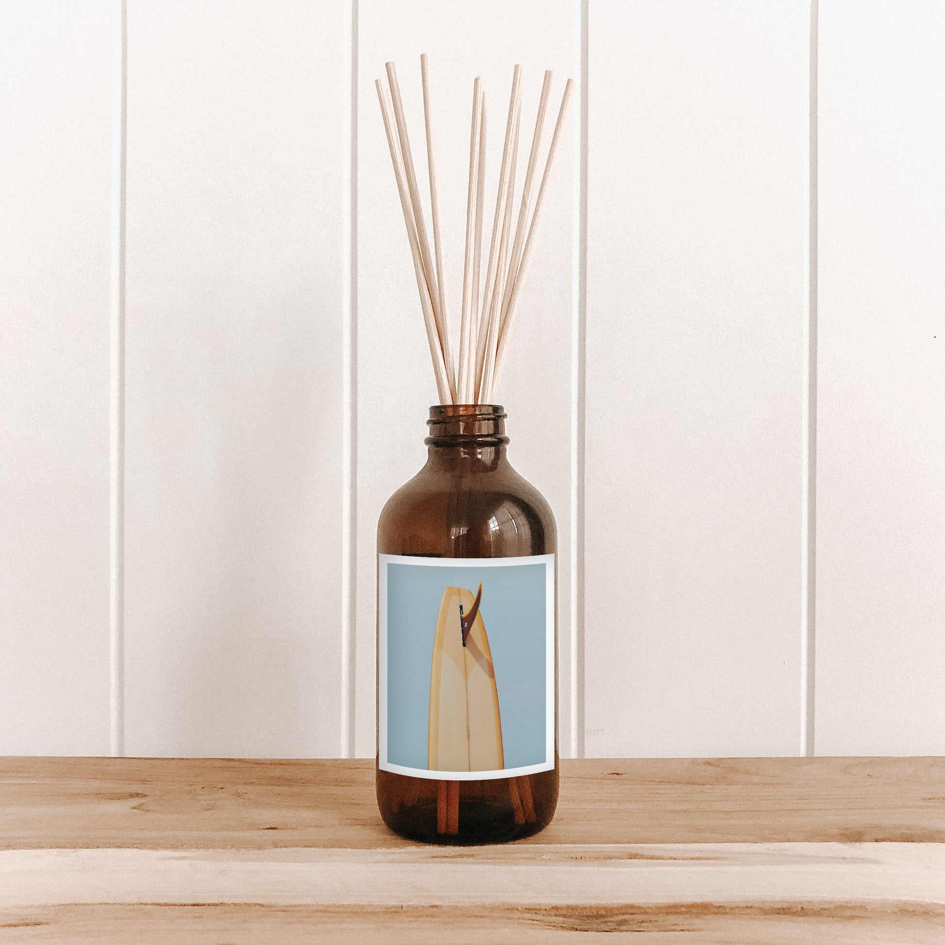 The Commonfolk room diffuser with a blue label and print of a mustard tail on a wooden surface and white paneled wall background 
