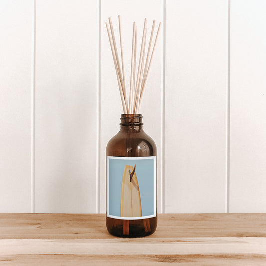 The Commonfolk room diffuser with a blue label and print of a mustard tail on a wooden surface and white paneled wall background 