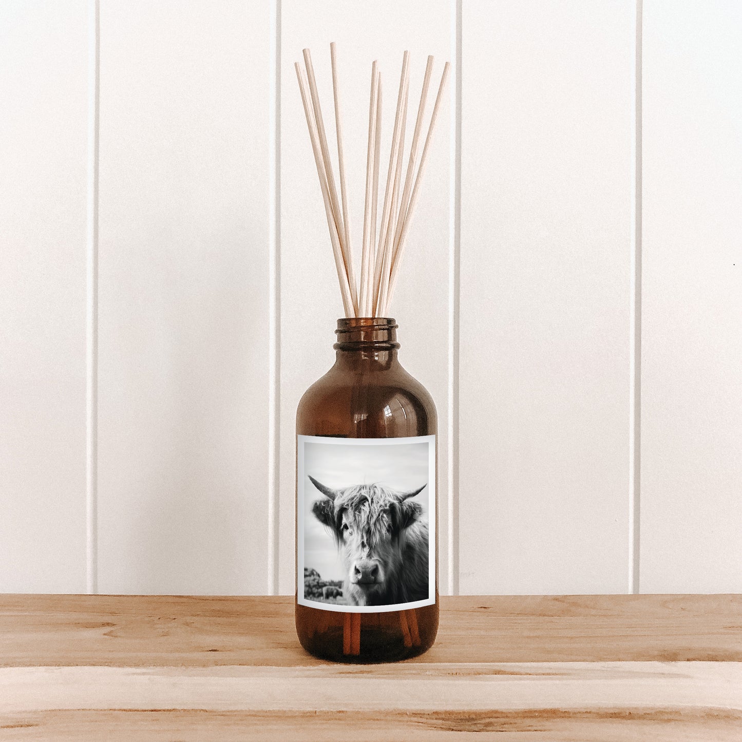 The Commonfolk room diffuser with a cow design and a label of wooden sticks on a white wall background.