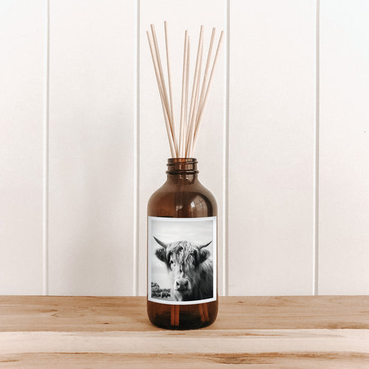 The Commonfolk room diffuser with a cow design and a label of wooden sticks on a white wall background.
