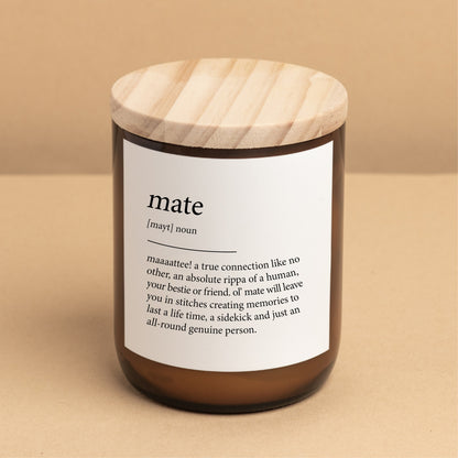 The Commonfolk scented candle with a wooden lid, labeled 'mate' with a definition in brackets, is placed on a beige background.